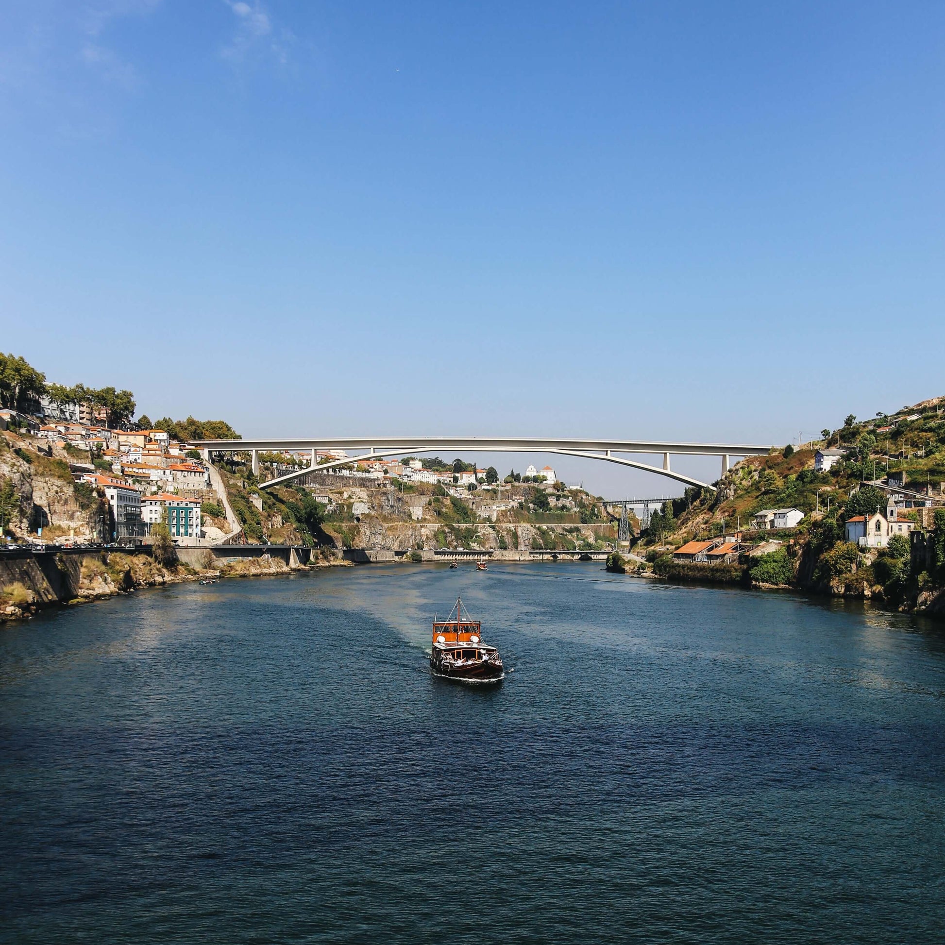 River scene with a boat and a bridge in the background under a clear blue sky.